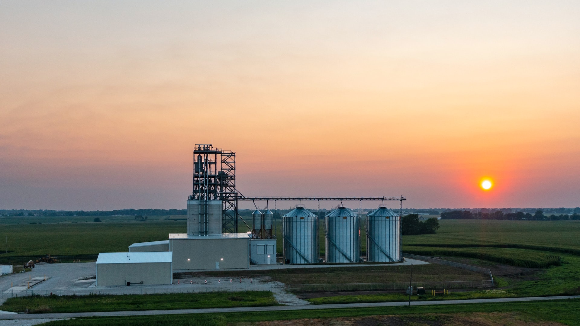 In the vast field landscape, a structure is dominated by three large silo-shaped tanks.