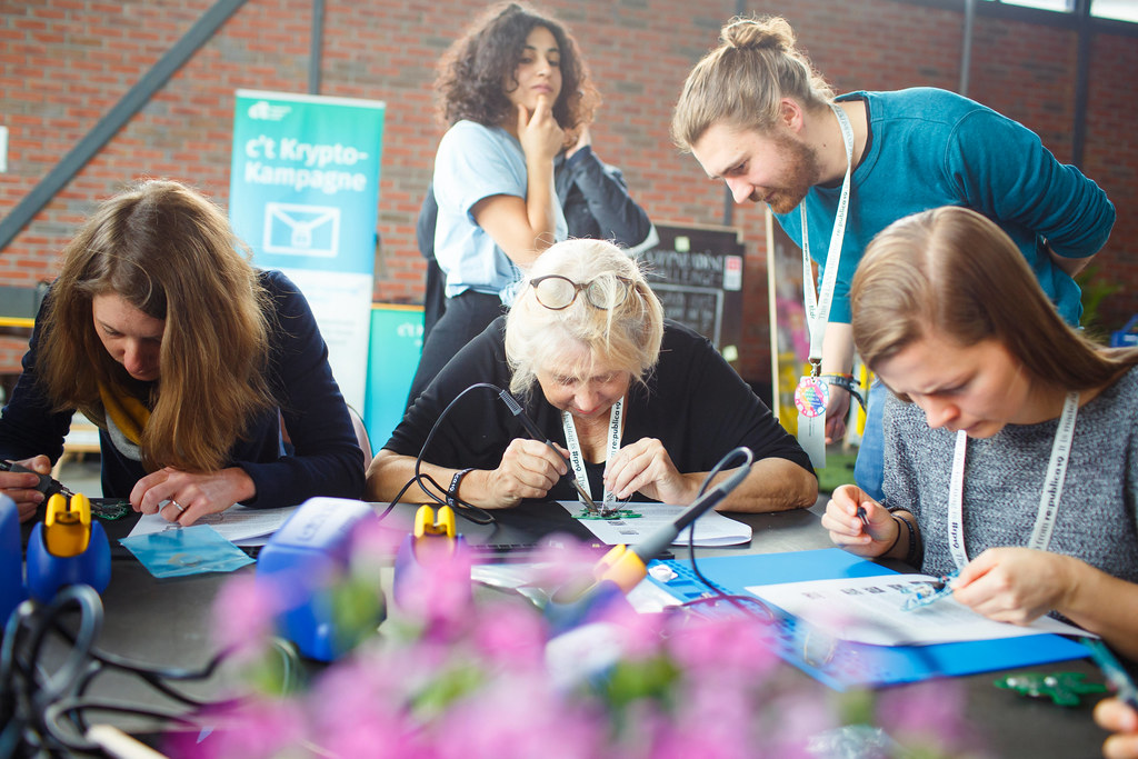 Three persons are diligently soldering circuit boards at a table. 